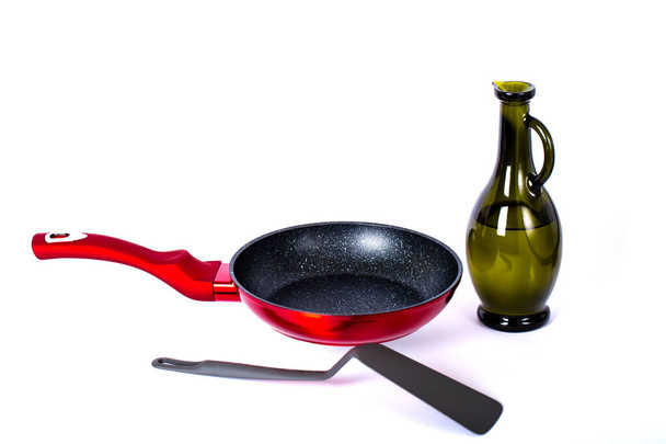 Glass carafe, red frying pan and kitchen spatula on a white background. Side view with copy space for your text. Studio shot, selective focus. Kitchen tools. Kitchenware. Cookware. Modern, domestic. - Photo, Image