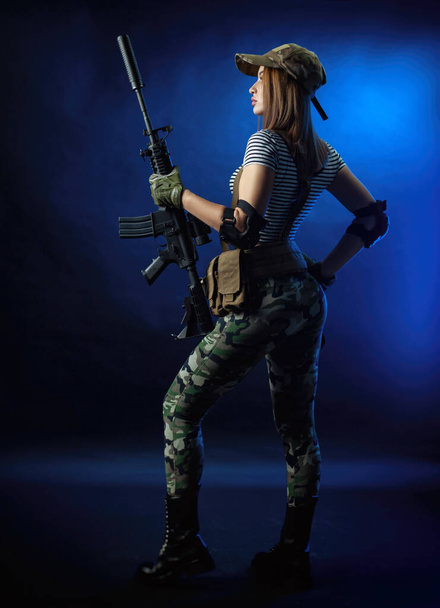 Sotilaspukuinen nainen liivissä, jolla on amerikkalainen automaattikivääri tummalla pohjalla. - Valokuva, kuva
