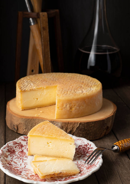 Moody brazilian Canastra artisanal cheese with slices over a wooden board with wine bottle. - Photo, Image