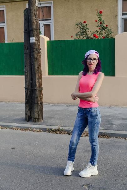 Молода кавказька жінка одягнена в рожеву сорочку і джинси, дивлячись на камеру з упевненістю і інтересом до теплого вечірнього світла - Фото, зображення