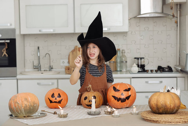 Счастливого Хэллоуина. Милая маленькая девочка в костюме ведьмы с вырезанной тыквой. Счастливая семья готовится к Хэллоуину. девушка зажигает свечи. - Фото, изображение