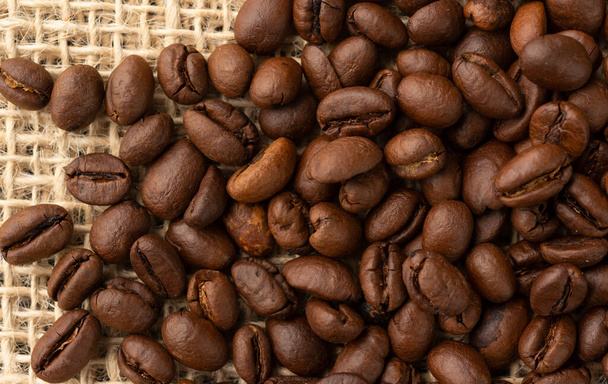 Closeup, top view of coffee beans over rustic bag. - Photo, Image