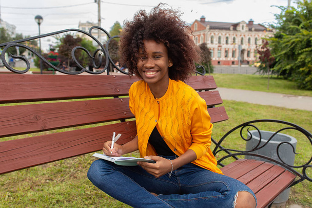 the Beautiful and happy African American woman in the park, makes notes in a notebook - Photo, image