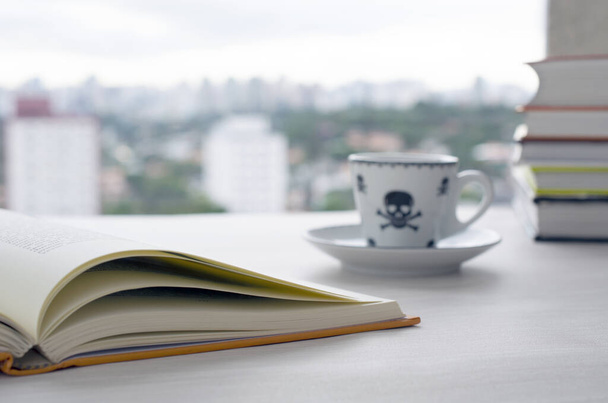 オープンブック、コーヒーカップ、木製のテーブルの上の本の山の風景曇りの背景. - 写真・画像