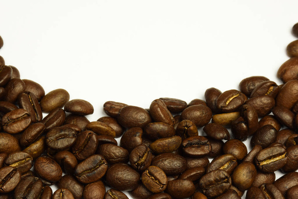 Roasted coffee grains scattered in a semicircle on a white background. The top side of the photo is blank for an inscription. Close-up photographed. - Foto, afbeelding
