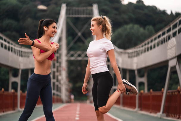 Happy two attractive young sportswomen standing outdoors and making sport training outdoors while talking. Fitness and lifestyle concept - Fotoğraf, Görsel
