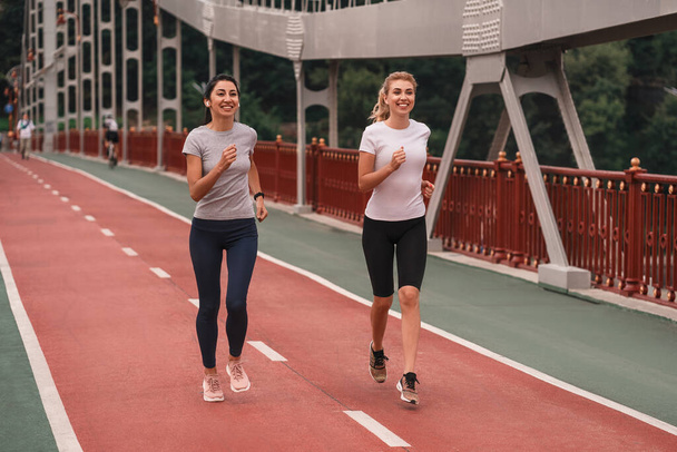 Spor giyimli mutlu genç bayanların sabahları şehirde koşarken çekilmiş uzun bir fotoğrafı. Sağlık ve spor konsepti - Fotoğraf, Görsel