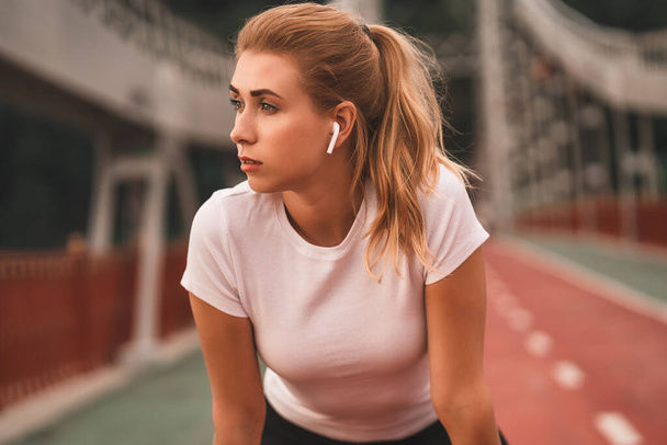 Portrait of pretty young fit lady having a break from her daily running session while staying on the bridge in the city. Sport concept - Φωτογραφία, εικόνα