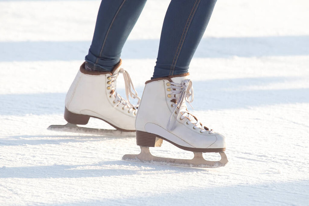 piernas de una mujer en pantalones vaqueros azules y patines blancos en una pista de hielo. pasatiempos y ocio. deporte de invierno - Foto, imagen