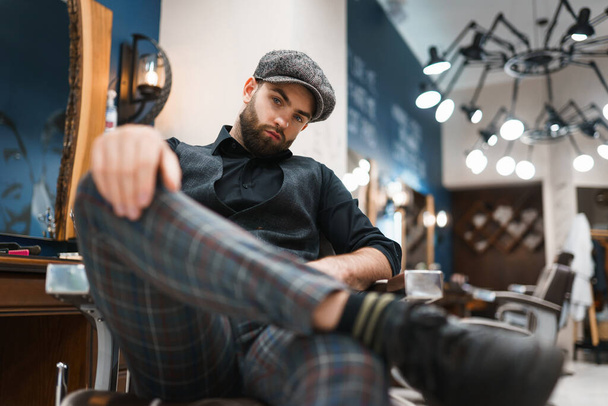 Stylishly dressed barber sits on chair in the salon - Photo, Image