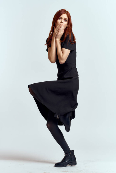 Nainen mustassa mekossa kevyellä taustalla ja sukkahousut kengät punaiset hiukset ja aiheuttavat täyden kasvun - Valokuva, kuva