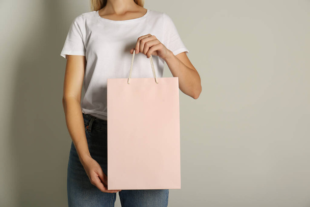 Woman with paper shopping bag on light grey background, closeup - Фото, изображение