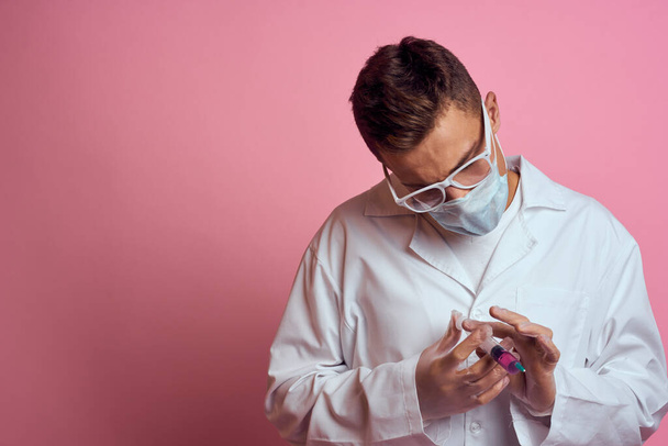 Un médico con una máscara médica y guantes sostiene una jeringa en las manos de un laboratorio de inyección - Foto, imagen
