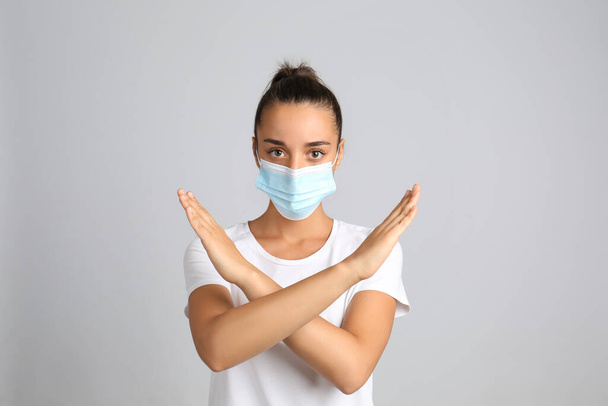Woman in protective mask showing stop gesture on grey background. Prevent spreading of COVID?19 - Фото, зображення