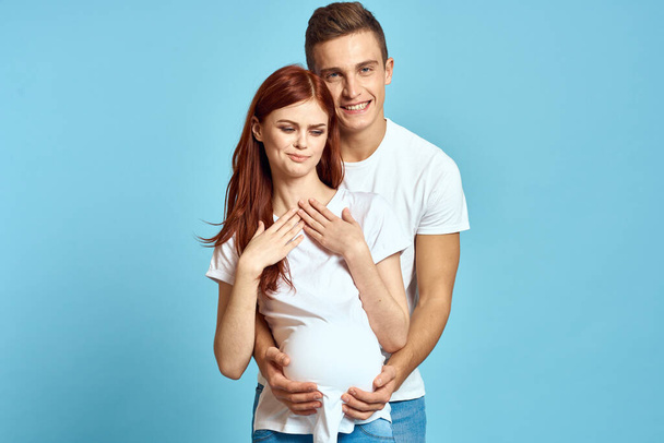 Kobieta w ciąży w białej koszulce i mężczyzna małżeństwo czeka na dziecko niebieskie tło przycięte widok emocji - Zdjęcie, obraz