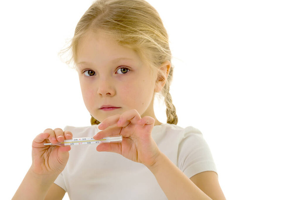 A little girl in a clean white T-shirt holds a thermometer in her hand. Covid-19 concept, virus, disease, treatment. - Foto, immagini