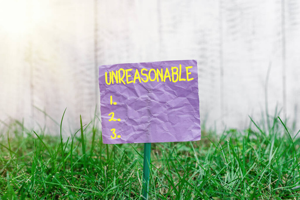 Conceptual hand writing showing Unreasonable. Business photo text not conformable to reason or exceeding the bounds of reason Plain paper attached to stick and placed in the grassy land. - Photo, Image