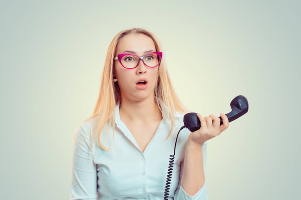 Confused puzzled young woman received bad news holding the phone down isolated on light green yellow background with copy space. Shocked stunned human emotion, face expression, reaction, feeling. - 写真・画像