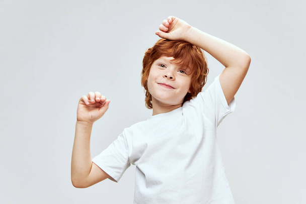 Veselý rudovlasý chlapec drží ruce na hlavě bílé tričko kfk šedé pozadí  - Fotografie, Obrázek