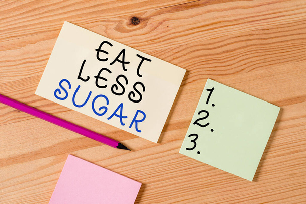 砂糖が少ないことを示すテキスト記号。概念的な写真砂糖摂取量を削減し、健康的な食事豊富な食品を食べる色の布紙空のリマインダ木製の床の背景オフィス. - 写真・画像