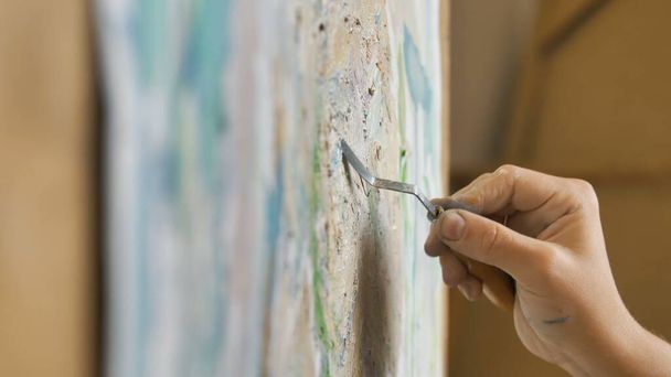 Artist applies oil paint on canvas with spatula in studio - 写真・画像
