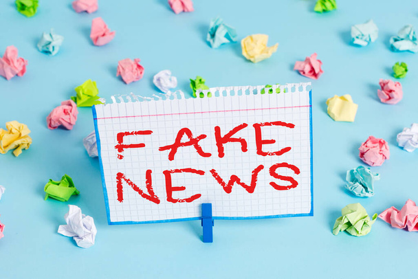 Handwriting text Fake News. Concept meaning false information publish under the guise of being authentic news Colored crumpled papers empty reminder blue floor background clothespin. - Photo, Image