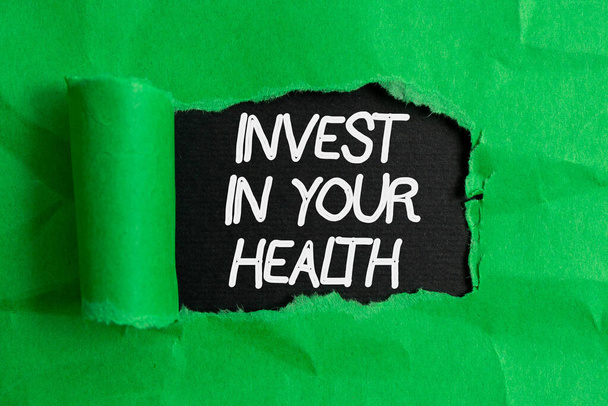 Handwriting text writing Invest In Your Health. Concept meaning put money on maintenance or improvement of your health Rolled ripped torn cardboard placed above a wooden classic table backdrop. - Photo, Image