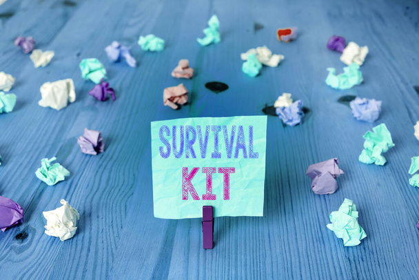 Survival Kit 'i gösteren bir not yazıyorum. Birisinin Renklendirilmiş Buruşuk dikdörtgen şekilli hatırlatıcı kağıt açık mavi arkaplan için acil durum ekipmanları koleksiyonunu gösteren iş fotoğrafı. - Fotoğraf, Görsel