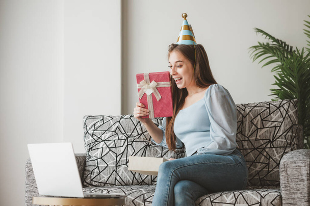 Happy woman opening geschenkdoos cadeau en gevoel verrast tijdens nieuwe normale online kerst feest thuis op de bank via laptop  - Foto, afbeelding