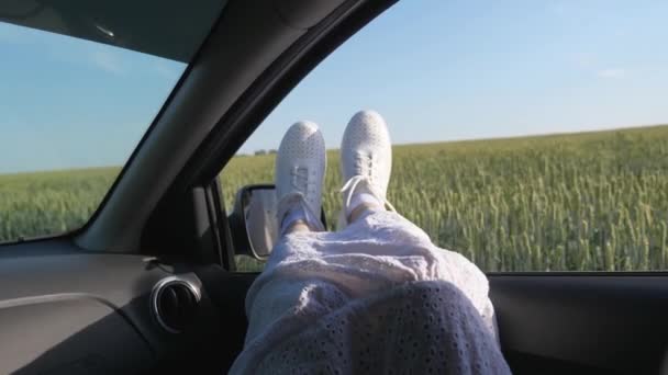 Legs of a girl in car window, riding car on country road past wheat field. free woman travels by car. healthy Young woman enjoys traveling by car, protruding her legs from an open window. travel - Footage, Video