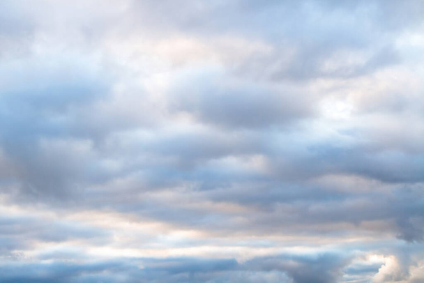 Schöner Himmel an einem bewölkten Tag mit blauen und violetten Schattierungen auf Kumuluswolken. Bewölktes Wetter am Herbstabend. Helle Wolkenlandschaft mit weißen Sonnenflecken, die durch die flauschigen Wolken ziehen. - Foto, Bild