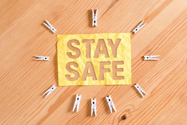 Stay Safe 'i gösteren bir not yazıyorum. İş fotoğrafı sergisi tehlike, zarar veya makaleleri saklamak için güvenli bir yer Renkli çamaşır iğnesi kağıtları boş ahşap zemin ofisini anımsatıyor. - Fotoğraf, Görsel