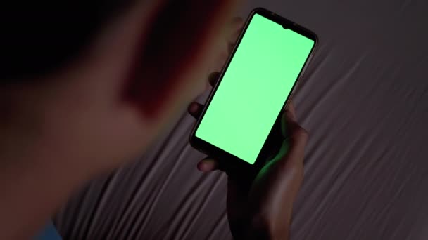 Man in het donker op bed Houdt en onderzoekt Smartphone met Green Touchscreen. - Video