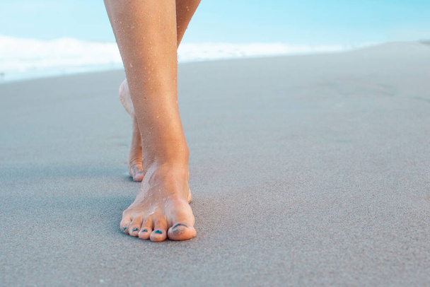 Kobieta spacerująca po piaskowej plaży zostawiając ślady stóp na piasku. Piękno, zdrowie, koncepcja pielęgnacji skóry. - Zdjęcie, obraz