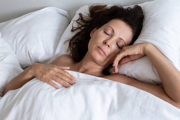 Schöne junge brünette Frau schläft in einem weißen Bett. - Foto, Bild