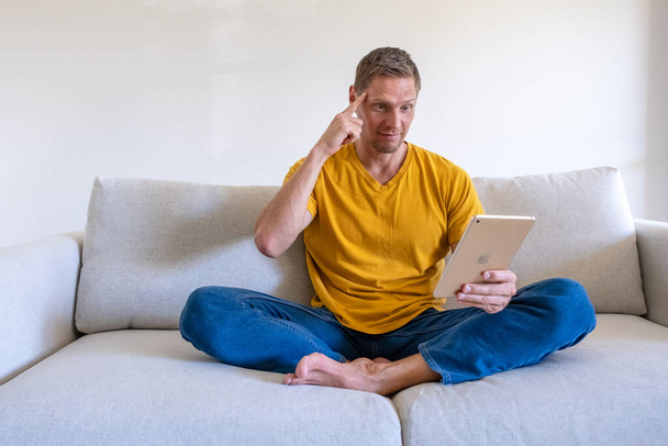 Handsome smiling man using tablet for video calling while relaxing on the couch. Concept for young business people working at home. - Fotoğraf, Görsel