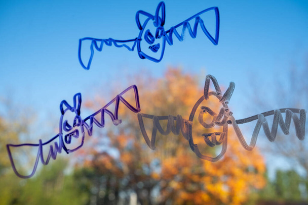 Σχέδια νυχτερίδων βαμπίρ που έγιναν από ένα παιδί σε δείκτη κοσμούν ένα παράθυρο τον Οκτώβριο, συμβολίζοντας μια εσωτερική Απόκριες για το 2020. - Φωτογραφία, εικόνα