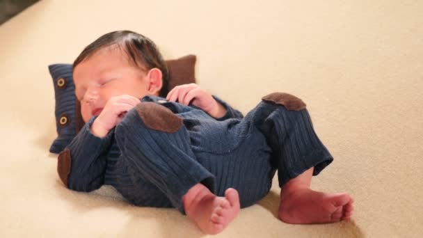 Lapsuus, lapsuus, vanhemmuus, äitiys. Suloinen ja söpö 10 päivän vastasyntynyt poika makaa tyynyllä neulotussa puvussa, irvistelee, haukottelee, tekee kasvoja, liikkuu jalat. 4 k video - Materiaali, video