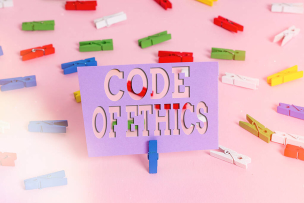 Handwriting text writing Code Of Ethics. Concept meaning basic guide for professional conduct and imposes duties Colored clothespin papers empty reminder pink floor background office pin. - Photo, Image