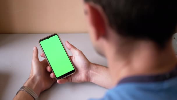 Mies pitää älypuhelinta, jossa on vihreä kosketusnäyttö pöydällä. Etsitään näyttöä - Materiaali, video
