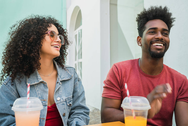 Portrait of two Afro friends having fun together and enjoying good time while drinking fresh fruit juice outdoors at cafeteria. - 写真・画像