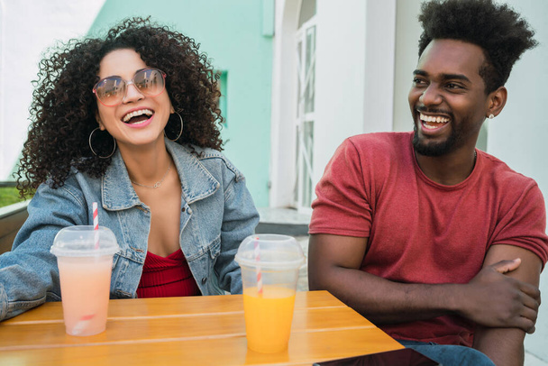 Portrait of two Afro friends having fun together and enjoying good time while drinking fresh fruit juice outdoors at cafeteria. - Фото, изображение