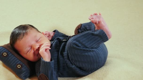 Imádnivaló, aranyos, 10 napos újszülött fiú, aki kötött öltönyben alszik a párnán a fotózónában, grimaszol, ásít és arcokat vág. Gyerekkor, gyerekkor, szülőség, anyaság. 4 k videó - Felvétel, videó