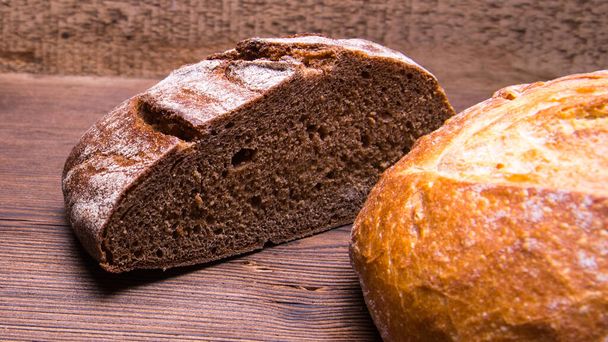 Pół bochenka chleba żytniego i cały bochenek białego chleba na starym drewnianym stole, zbliżenie - Zdjęcie, obraz