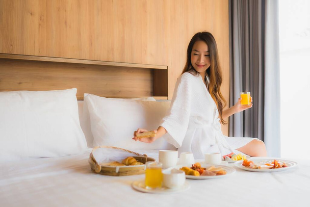 Portret piękna młoda azjatycka kobieta szczęśliwy cieszyć się śniadaniem na łóżku we wnętrzu sypialni - Zdjęcie, obraz