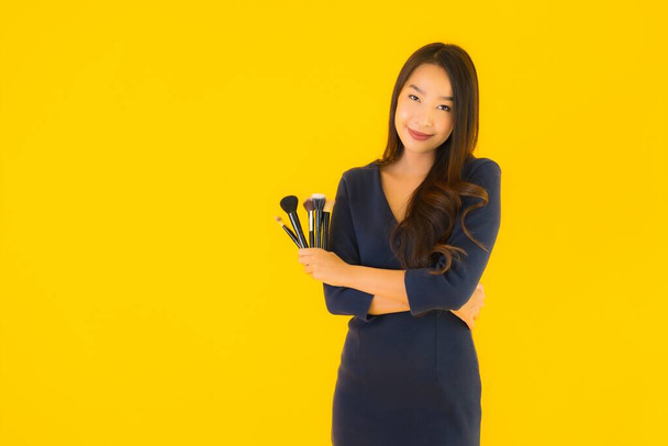 Portrait beautiful young asian woman with makeup brush on yellow isolated background - Foto, afbeelding