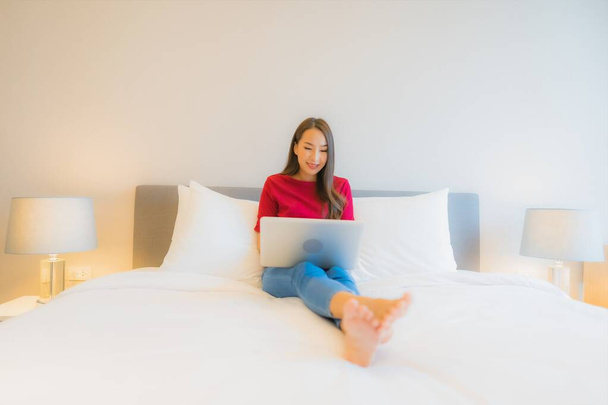 Портрет красивая молодая азиатская женщина использовать ноутбук на кровати в интерьере спальни - Фото, изображение