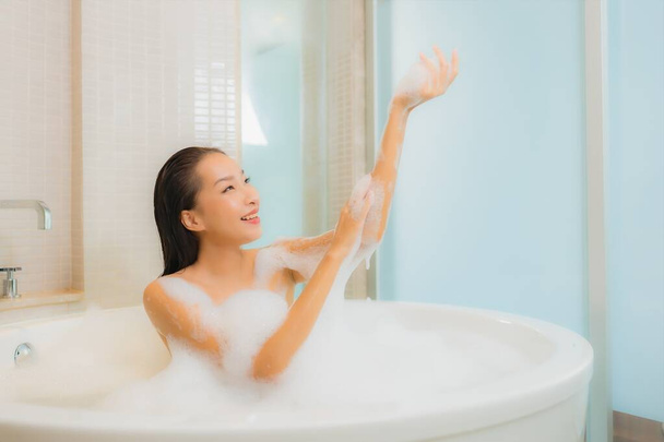 Portrait belle jeune femme asiatique se détendre sourire dans la baignoire à l'intérieur de la salle de bain - Photo, image