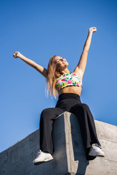 Νεαρή γυναίκα ανοίγει τα χέρια της στον γαλάζιο ουρανό - Φωτογραφία, εικόνα