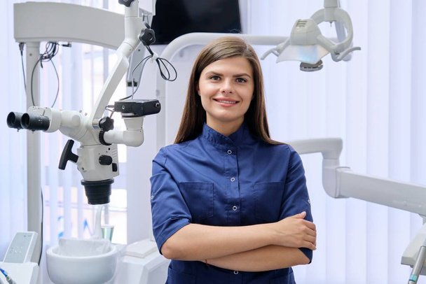 Portrait of young confident female dentist doctor with folded hands in dental office. - Photo, Image